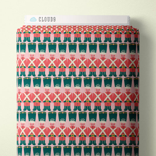 Fabric with a pattern of toy soldiers wearing red coats with green boots on a pink background, branded 'Cloud9'.