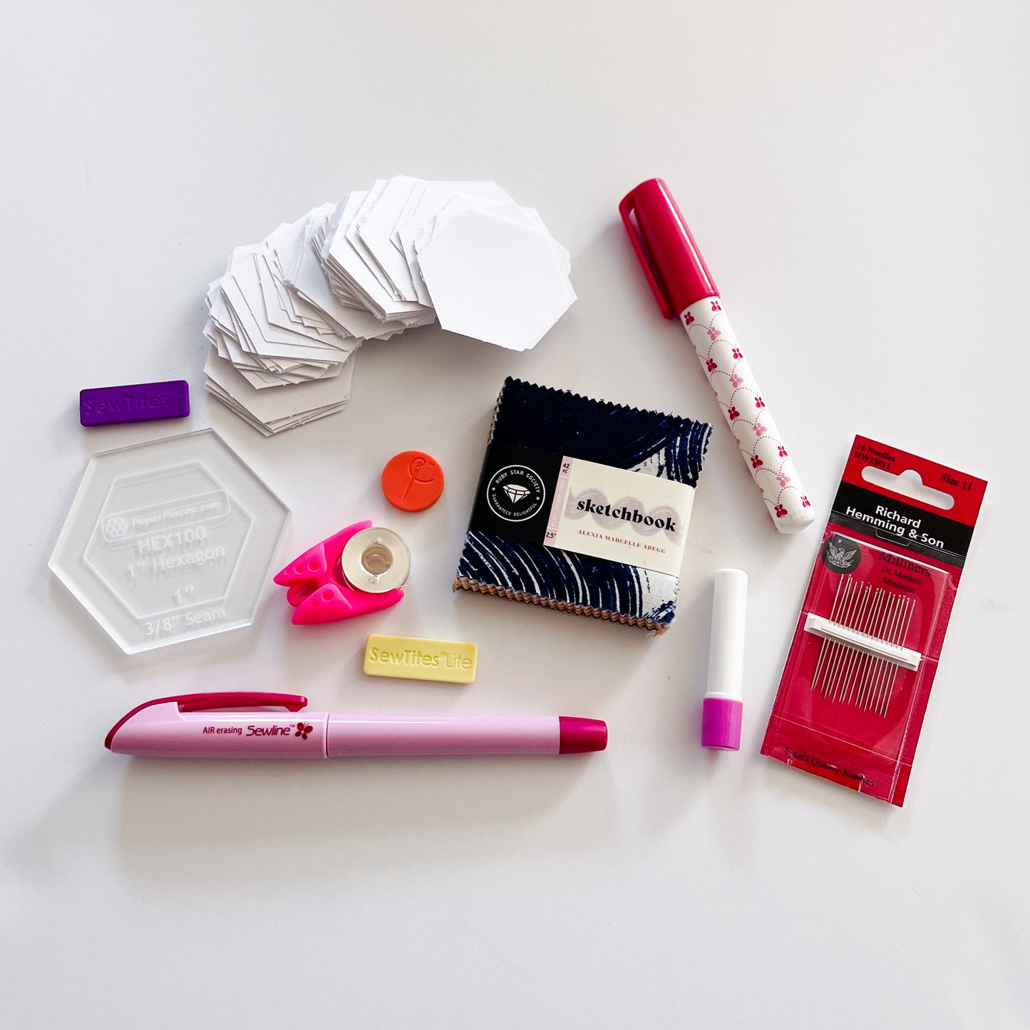 Essential supplies for English Paper Piecing including paper hexagons, hexagon template, sewline glue pen, milliners needles, sewtites magnetic pins, and an air erasable pen for tracing your fussy cuts. The EPP kit also includes a mini charm pack.