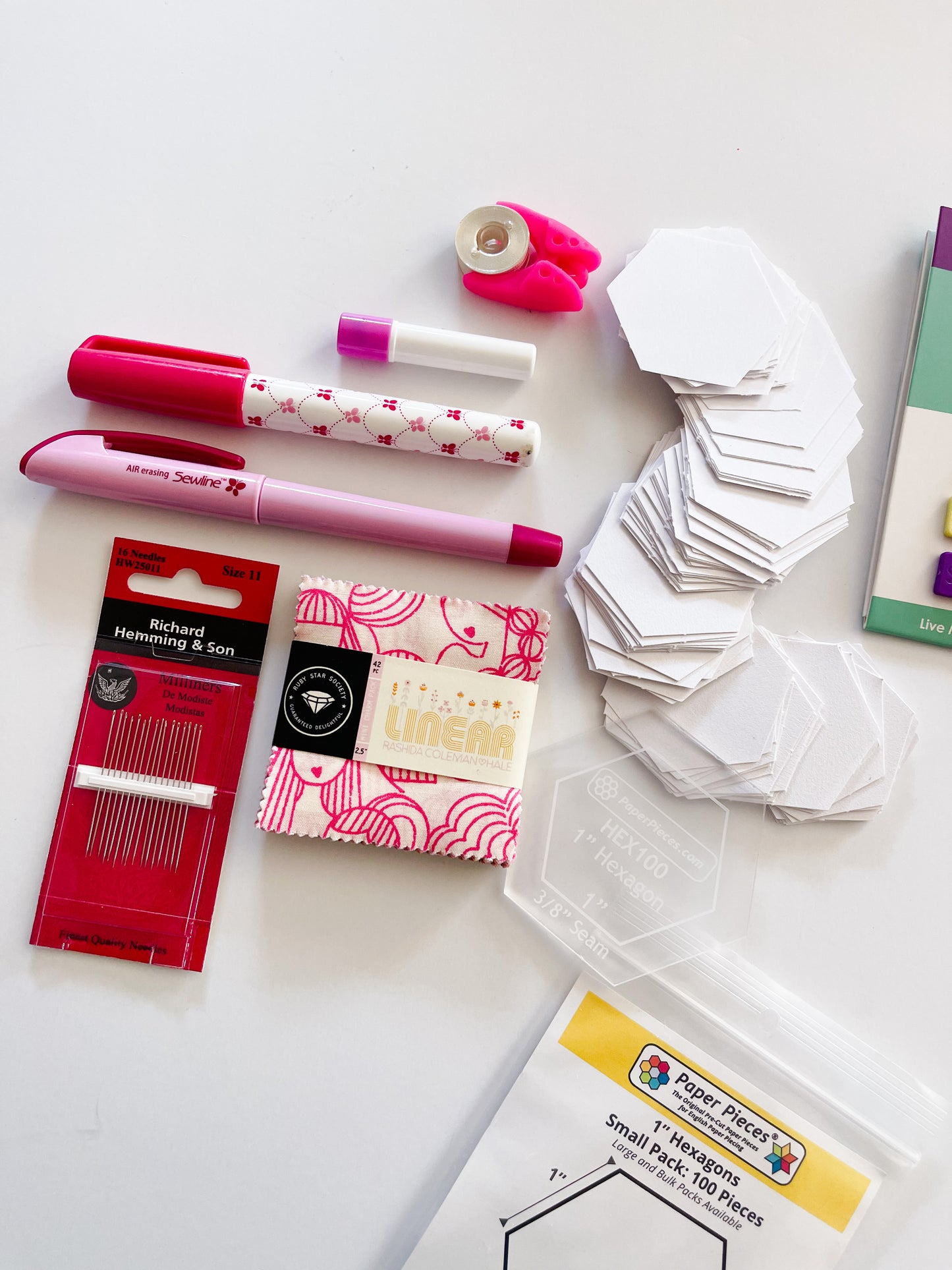 Essential supplies for English Paper Piecing including paper hexagons, hexagon template, sewline glue pen, milliners needles, sewtites magnetic pins, and an air erasable pen for tracing your fussy cuts. The EPP kit also includes a mini charm pack.