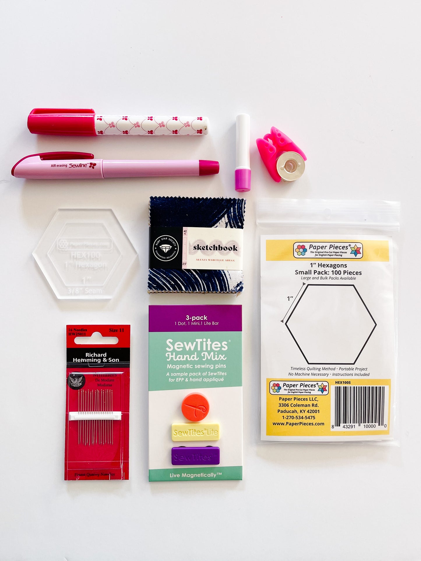 Essential supplies for English Paper Piecing including paper hexagons, hexagon template, sewline glue pen, milliners needles, sewtites magnetic pins, and an air erasable pen for tracing your fussy cuts. The EPP kit also includes a mini charm pack.